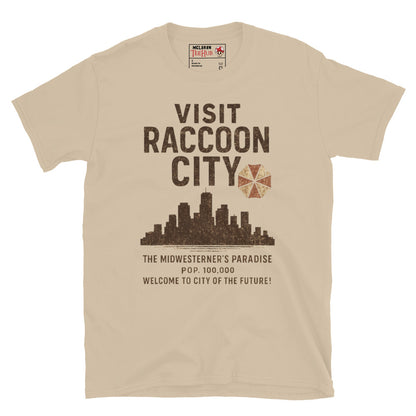 Sand T-shirt with vintage-style “Visit Raccoon City” graphic featuring city skyline, Umbrella Corp logo, and distressed text inspired by Resident Evil.