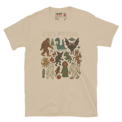 Sand T-shirt featuring vintage cartoon-style illustrations of various cryptids including Bigfoot, Mothman, Loch Ness Monster, and more.